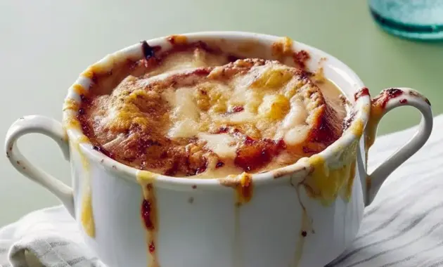French Onion Soup Recipe — steaming bowl of onion soup topped with a toasted baguette slice and bubbling, browned cheese under the broiler.