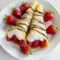 Close-up of stacked Sweet Crepes Recipe filled with sliced strawberries and whipped cream, drizzled with chocolate for a Strawberry Chocolate Crepes finish.