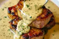 Pork Dishes Recipes — close-up of a maple-glazed pork chop topped with creamy Dijon sauce and crumbled bacon, garnished with fresh herbs.