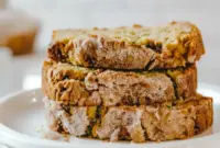 Loaf of Snickerdoodle Zucchini Bread on a wooden board, topped with a cinnamon-sugar Snickerdoodle Topping For Zucchini Bread, sliced to show a moist crumb.