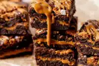 Biscoff Cookie Butter Brownies sliced into squares, revealing a rich chocolate layer, a creamy cookie-butter core, and crushed Biscoff cookies on top.