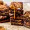 Biscoff Cookie Butter Brownies sliced into squares, revealing a rich chocolate layer, a creamy cookie-butter core, and crushed Biscoff cookies on top.