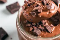 Jar of creamy High Protein Low Carb Snack protein pudding topped with a few nuts and cocoa nibs — a grab-and-go High Protein Low Carb Snack for post-workout or on-the-go fuel.