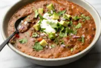 Steaming bowl of Black Bean Soup topped with cilantro, avocado, and a lime wedge — a simple Homemade Black Bean Soup ready in half an hour.