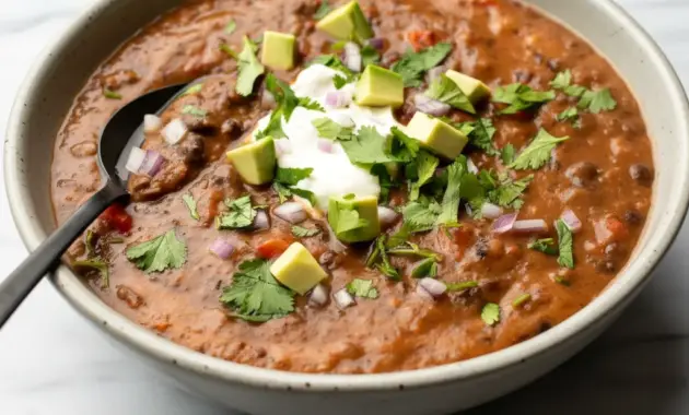 Steaming bowl of Black Bean Soup topped with cilantro, avocado, and a lime wedge — a simple Homemade Black Bean Soup ready in half an hour.