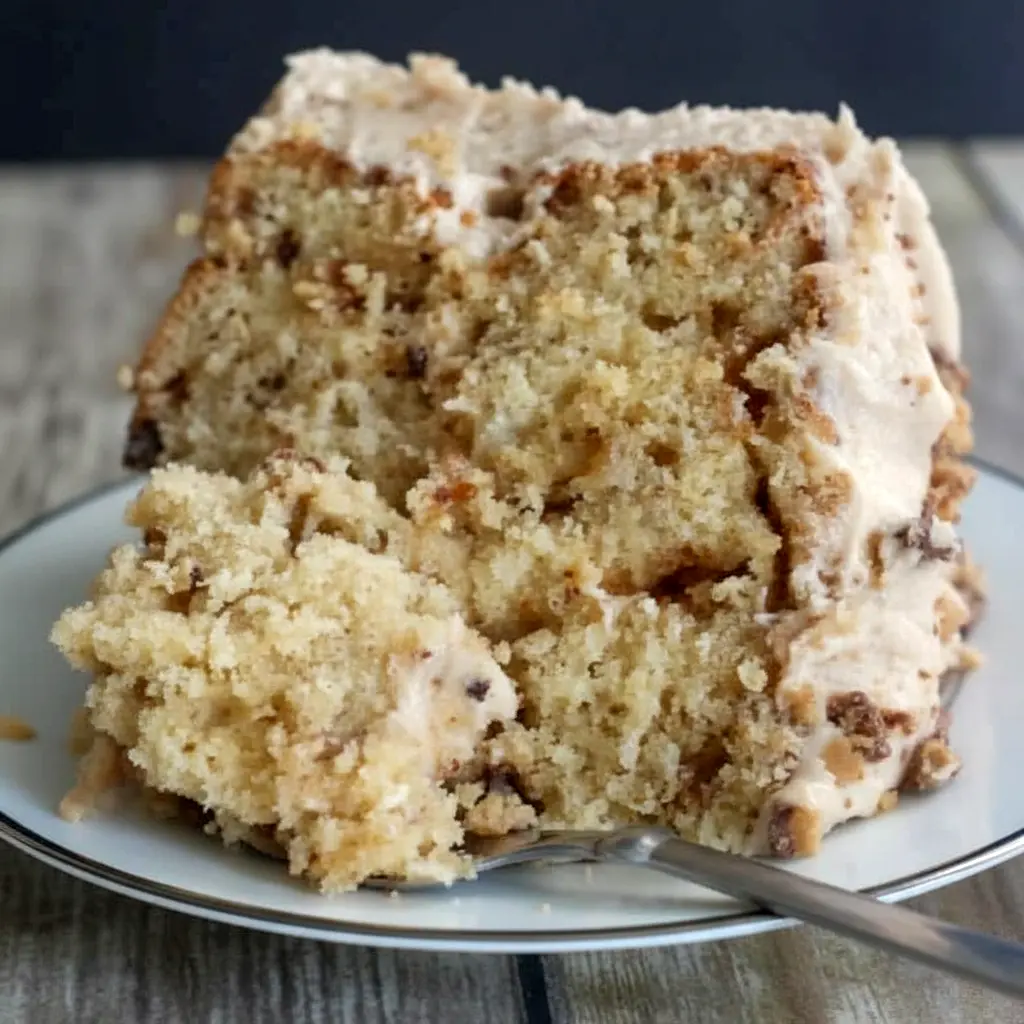 Banana Toffee Cake — slice showing banana-speckled crumb, glossy browned-butter toffee buttercream, and scattered toffee bits on top.