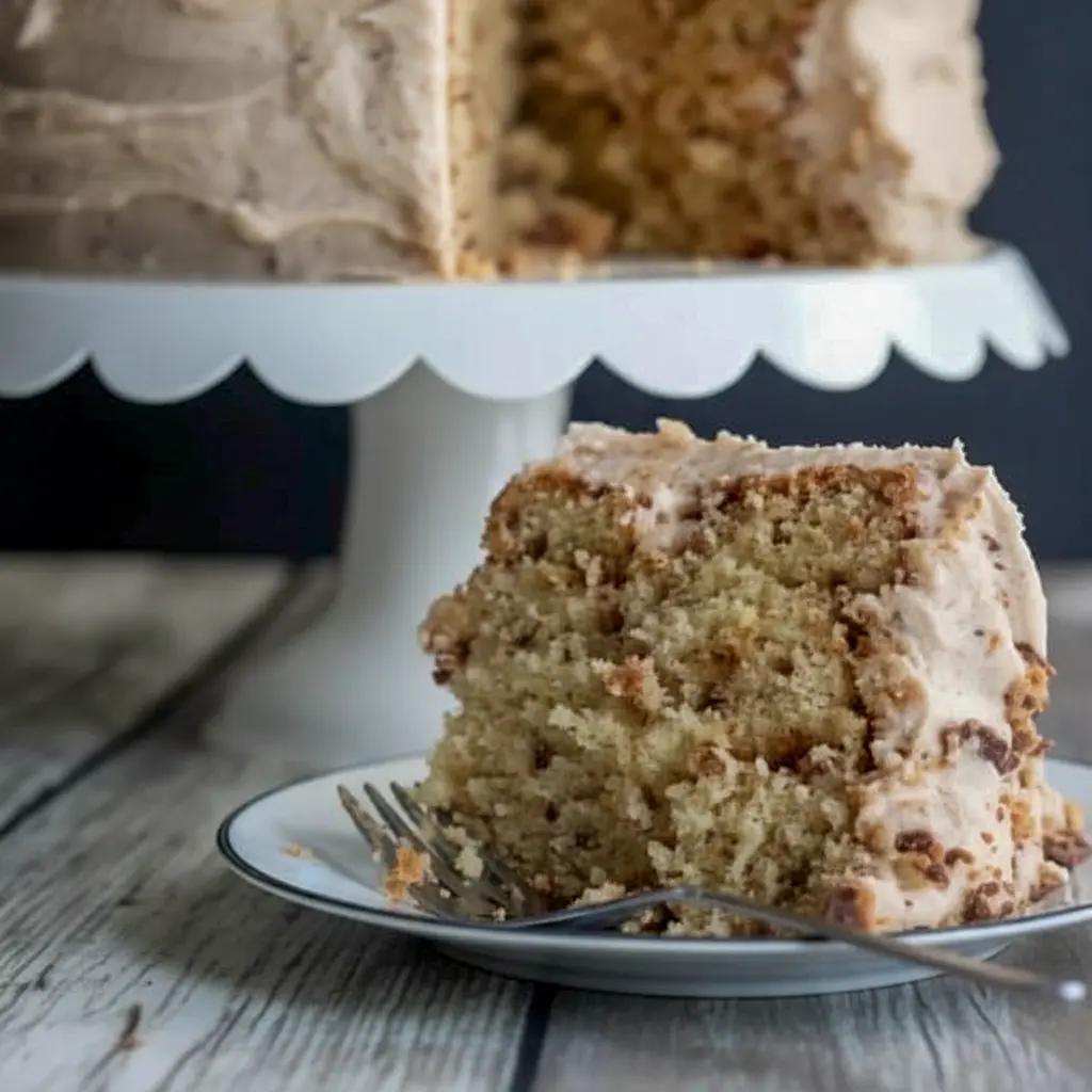 Banana Toffee Cake — slice showing banana-speckled crumb, glossy browned-butter toffee buttercream, and scattered toffee bits on top.