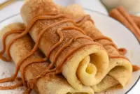 Plate of Cinnamon Roll Protein Crepes rolled and dusted with cinnamon, showing the creamy filling — a tasty example of Super Simple High Protein Meals.