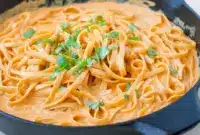 Plate of Red Pepper Alfredo Pasta — creamy red sauce coating fettuccine with a basil garnish, close-up overhead shot.