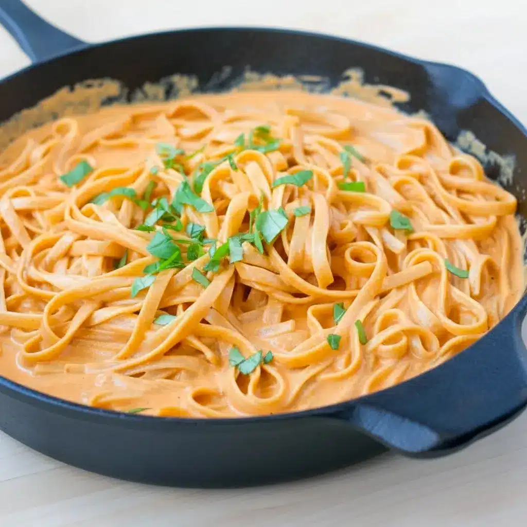 Plate of Red Pepper Alfredo Pasta — creamy red sauce coating fettuccine with a basil garnish, close-up overhead shot.