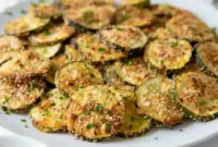 A plate of Crispy Baked Zucchini Chips with a crunchy golden coating, served as Healthy Baked Zucchini Snack with dipping sauce on the side.