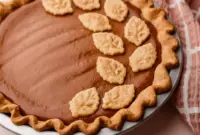 Slice of Apple Butter Pie on a plate with a dollop of maple whipped cream, showing creamy filling and a golden crust — a classic Fall Baking and Holiday Desserts favorite.