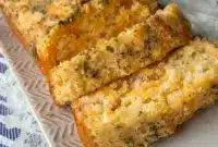 Loaf of Cheddar Bay Biscuit Bread sliced on a wooden board, topped with garlic-butter glaze and parsley — a delicious Side Bread Recipes option to pair with bowls of soup.