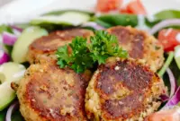 Close-up of golden Easy Falafel Recipe patties on a plate with pita, a bowl of tzatziki, and fresh parsley garnish.