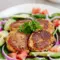 Close-up of golden Easy Falafel Recipe patties on a plate with pita, a bowl of tzatziki, and fresh parsley garnish.