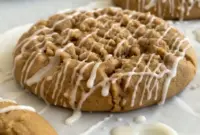 A close-up of Gilmore Girls Coffee Cake Cookies with golden edges, a soft center, cinnamon streusel topping, and vanilla icing, styled like cozy Coffee Cookies on a parchment-lined baking tray.