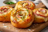 Golden Ham And Cheese pinwheels on a platter, flaky and savory — tasty Ham Appetizers for Easter or party spreads.