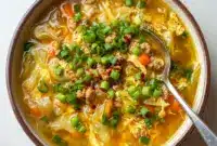 Steaming bowl of Egg Roll Soup with ground pork, shredded cabbage, carrots, and sliced green onions, ready to serve.