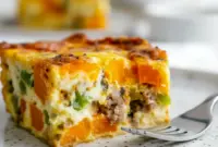Slice of golden Sweet Potato Egg Casserole showing sweet potato cubes, melted cheese, and sausage, garnished with herbs — a hearty Breakfast Potato Bake perfect for meal prep.