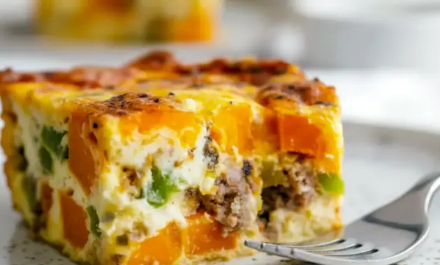 Slice of golden Sweet Potato Egg Casserole showing sweet potato cubes, melted cheese, and sausage, garnished with herbs — a hearty Breakfast Potato Bake perfect for meal prep.