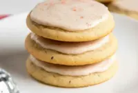 A stack of iced Taylor Swift Chai Cookies on a plate with a warm mug of tea, styled as a cozy homemade dessert.