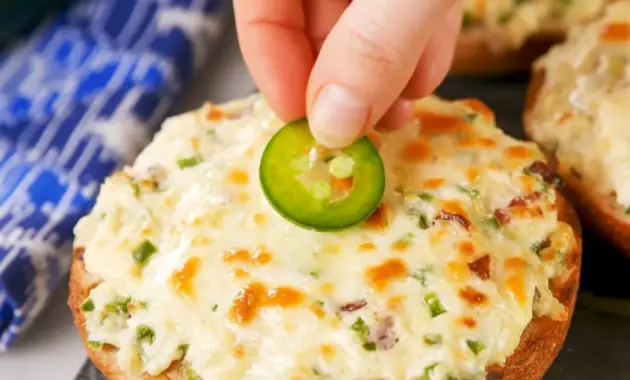 Close-up of baked Jalapeño Popper Bagels — bagel halves spread with jalapeño cream cheese, melted Monterey Jack, and bacon crumbles, garnished with thin jalapeño slices.