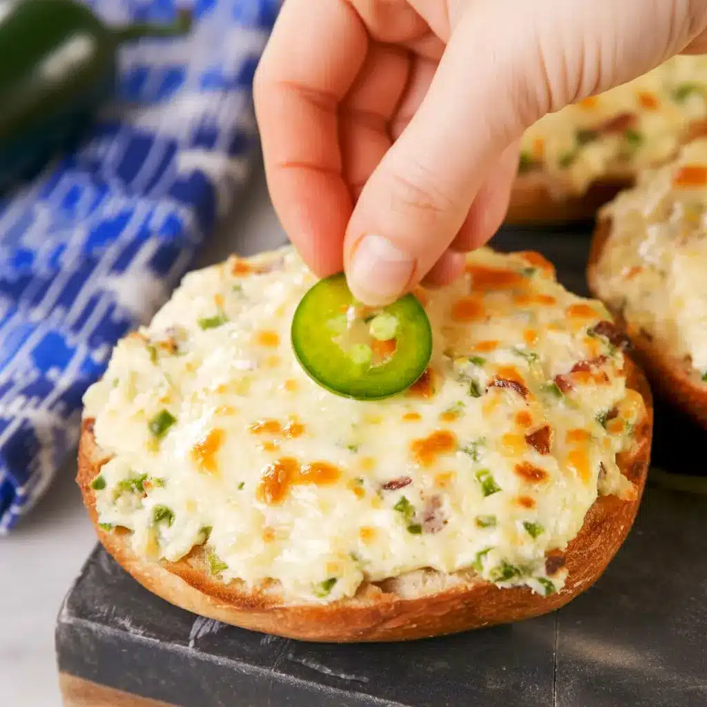 Close-up of baked Jalapeño Popper Bagels — bagel halves spread with jalapeño cream cheese, melted Monterey Jack, and bacon crumbles, garnished with thin jalapeño slices.