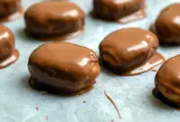 Close-up of Peanut Butter Protein Bars dipped in chocolate and cooling on parchment paper — chewy, chocolate-coated snack ready to eat.