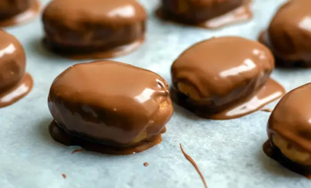 Close-up of Peanut Butter Protein Bars dipped in chocolate and cooling on parchment paper — chewy, chocolate-coated snack ready to eat.