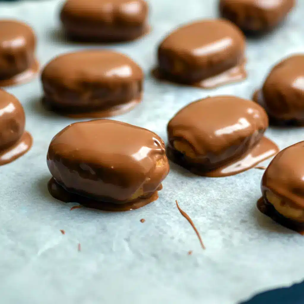Close-up of Peanut Butter Protein Bars dipped in chocolate and cooling on parchment paper — chewy, chocolate-coated snack ready to eat.