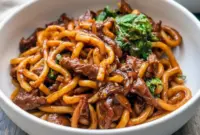 Bowl of Beef Udon with sliced steak, Chinese cabbage, and glossy black-pepper sauce over springy Noodles.