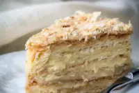 Russian Napoleon Cake slice with thin flaky pastry layers, rich custard filling, and a crumb-coated top on a serving plate.