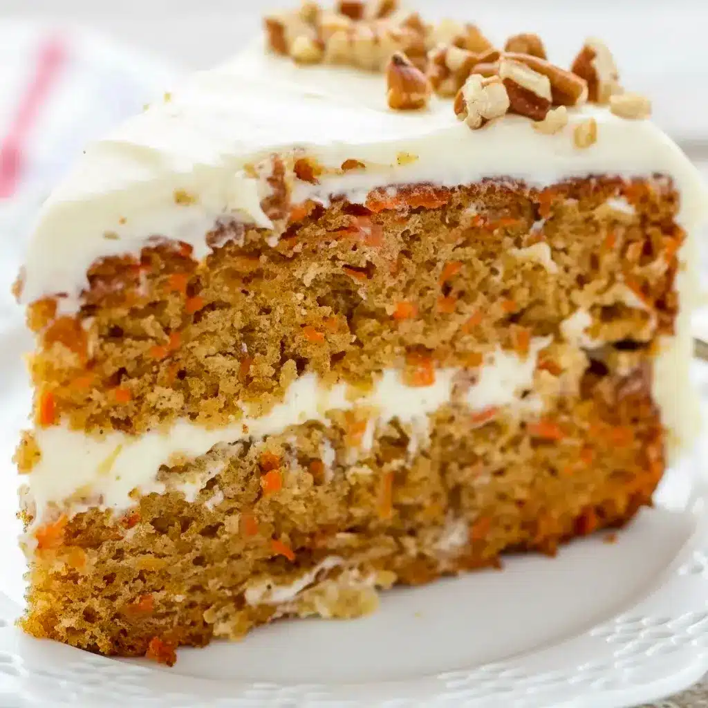 A beautifully layered Carrot Cake Recipe with fluffy Cream Cheese Frosting, featuring a thick slice that shows its tender crumb and rich texture. This Super Moist Carrot Cake is decorated with smooth frosting and simple carrot garnish, making it the perfect Easter Dessert or classic homemade cake for celebrations.