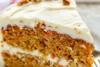 A beautifully layered Carrot Cake Recipe with fluffy Cream Cheese Frosting, featuring a thick slice that shows its tender crumb and rich texture. This Super Moist Carrot Cake is decorated with smooth frosting and simple carrot garnish, making it the perfect Easter Dessert or classic homemade cake for celebrations.