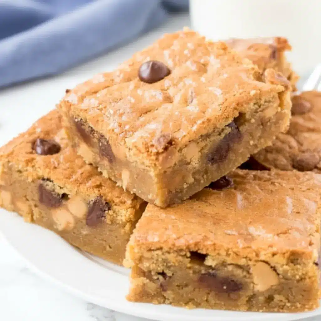 A close-up tray of Peanut Butter Blondies topped with Peanut Blondies style texture, loaded with Reese’s Pieces and chocolate chips, showing soft centers and chewy edges.