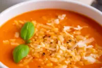 A bowl of High Protein Tomato Soup topped with basil and parmesan, styled as a comforting Creamy Healthy Soup.