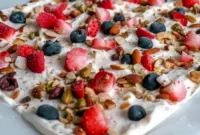 A sheet of Frozen Yogurt Bark topped with berries and nuts for a refreshing, crunchy, and colorful dessert.
