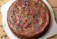 A rich slice of Cosmic Brownie Cheesecake for Creative Cooking Ideas, topped with glossy ganache and colorful candy-coated chips.