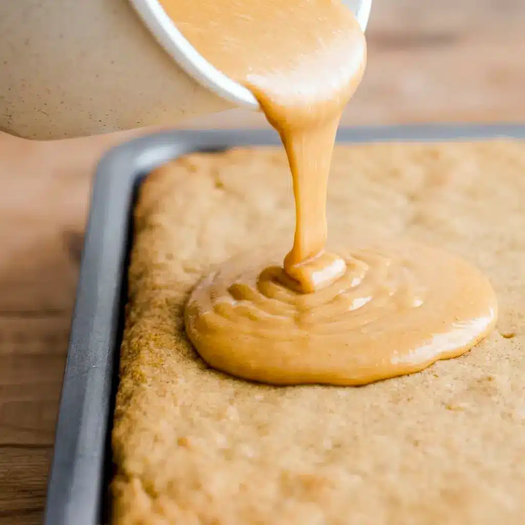 Hot coffee icing poured over a golden cake in a metal baking pan, showing how this Coffee Fudge Traybake gets its fudgy top.